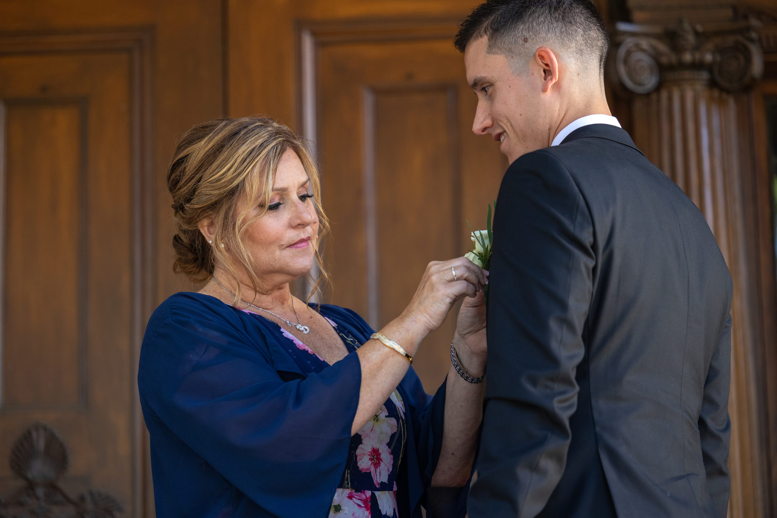 mom puts boutonnière on groom before wedding at Westmoreland Club